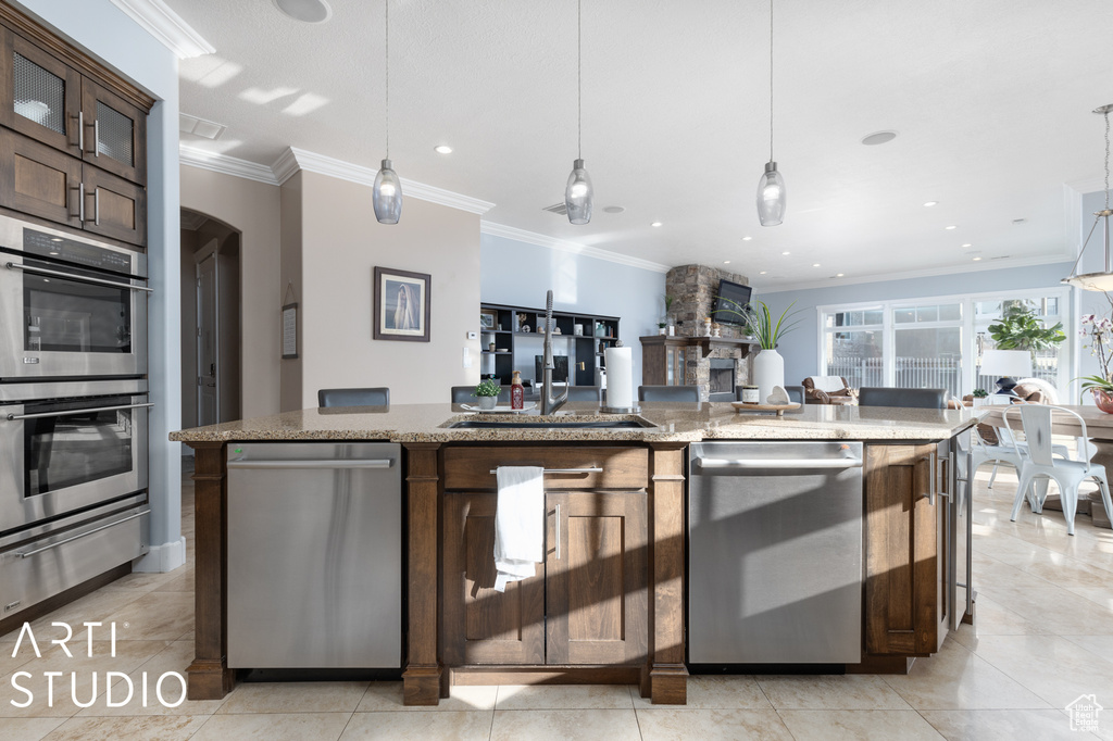 Kitchen featuring hanging light fixtures, stainless steel appliances, dark brown cabinets, and light stone countertops