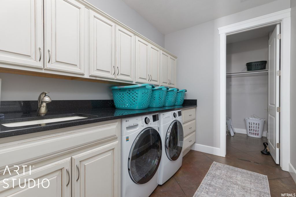 Laundry area with dark tile flooring, sink, washing machine and dryer, and cabinets