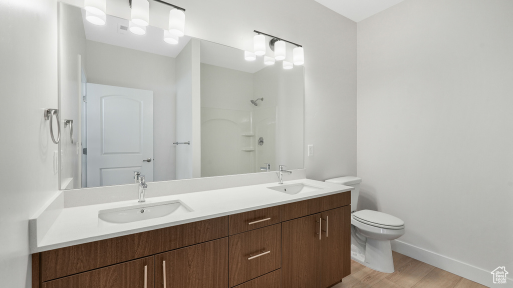 Bathroom featuring wood-type flooring, oversized vanity, toilet, and dual sinks