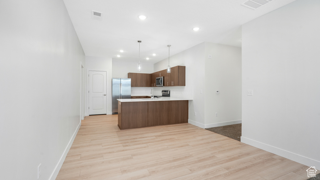 Kitchen with pendant lighting, stainless steel appliances, light hardwood / wood-style floors, and kitchen peninsula