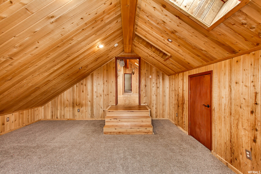 Additional living space featuring lofted ceiling with skylight, wooden walls, wooden ceiling, and light carpet