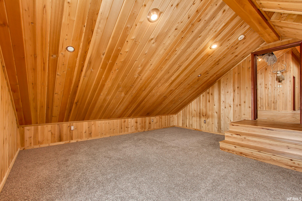 Additional living space featuring lofted ceiling, light carpet, and wooden walls