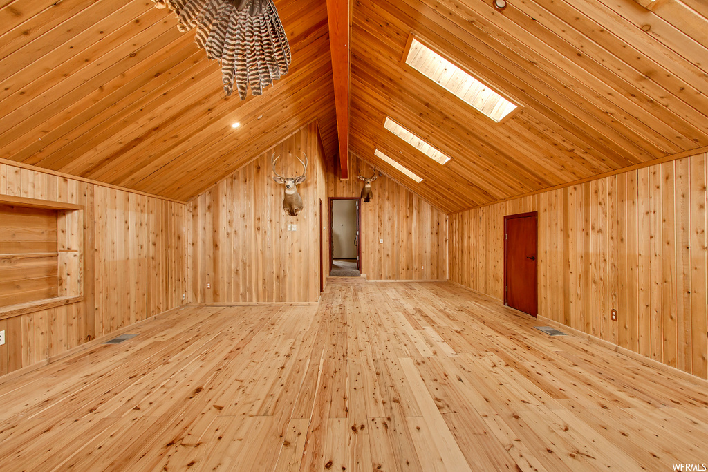 Bonus room featuring lofted ceiling with skylight, wooden walls, and light hardwood / wood-style floors