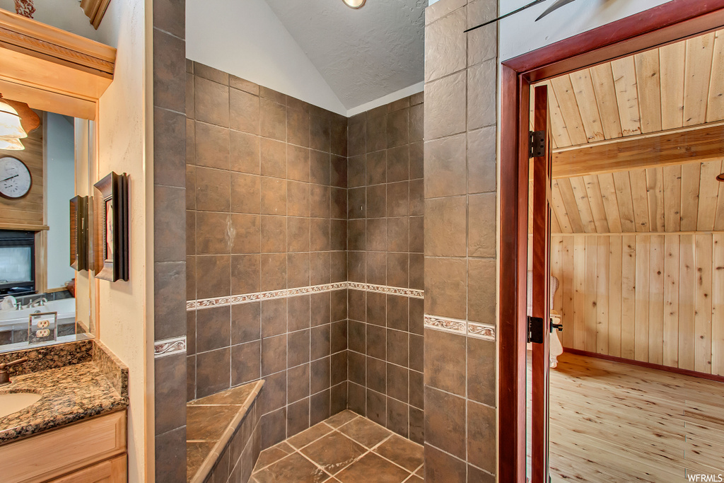 Bathroom with lofted ceiling, hardwood / wood-style floors, wooden walls, and vanity with extensive cabinet space