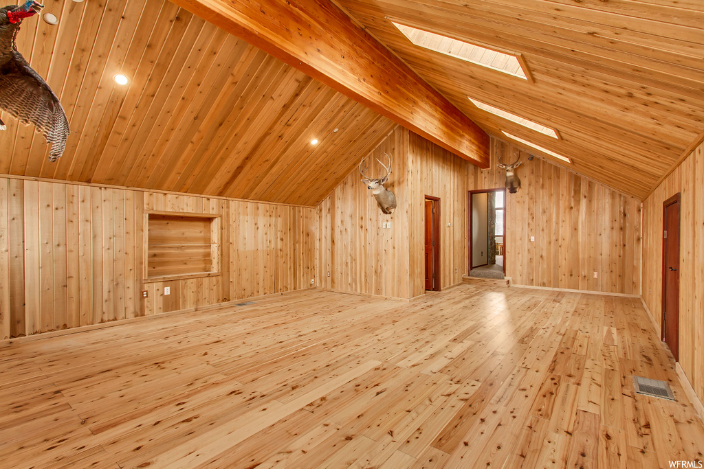 Bonus room with light hardwood / wood-style flooring, high vaulted ceiling, wood walls, a skylight, and beamed ceiling