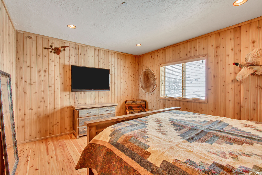 Bedroom featuring light hardwood / wood-style flooring, wooden walls, and a textured ceiling