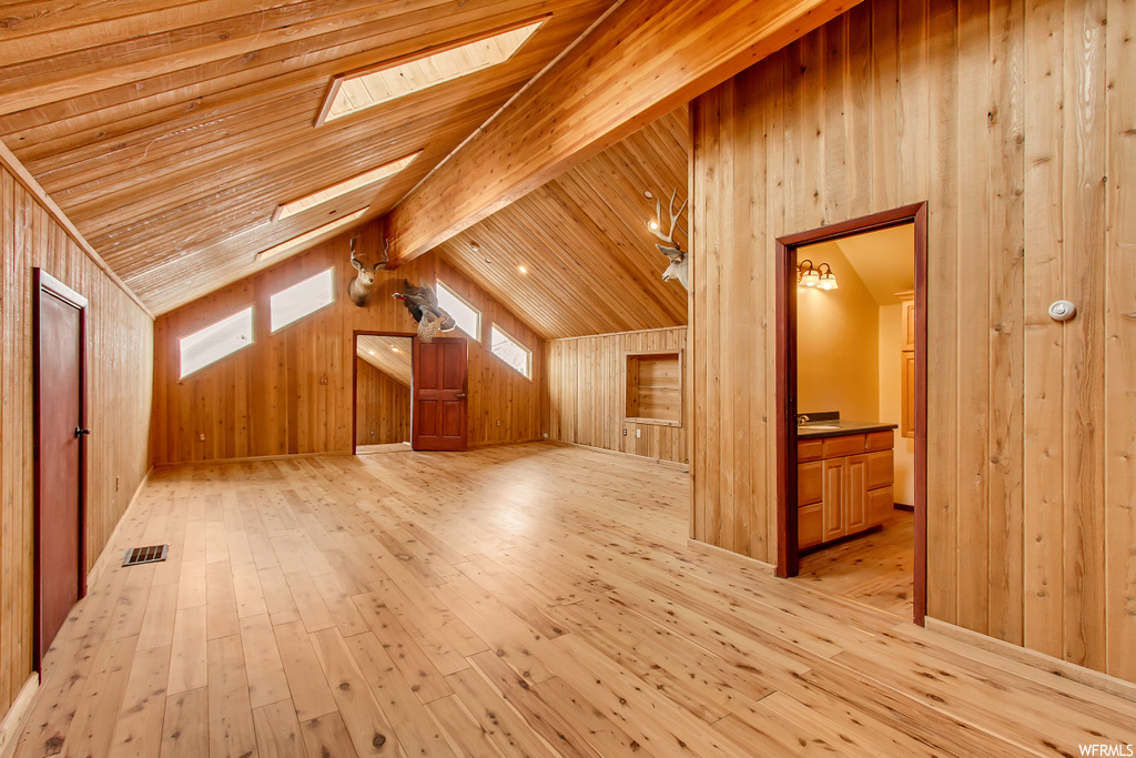 Bonus room featuring lofted ceiling with skylight, light wood-type flooring, and wooden walls