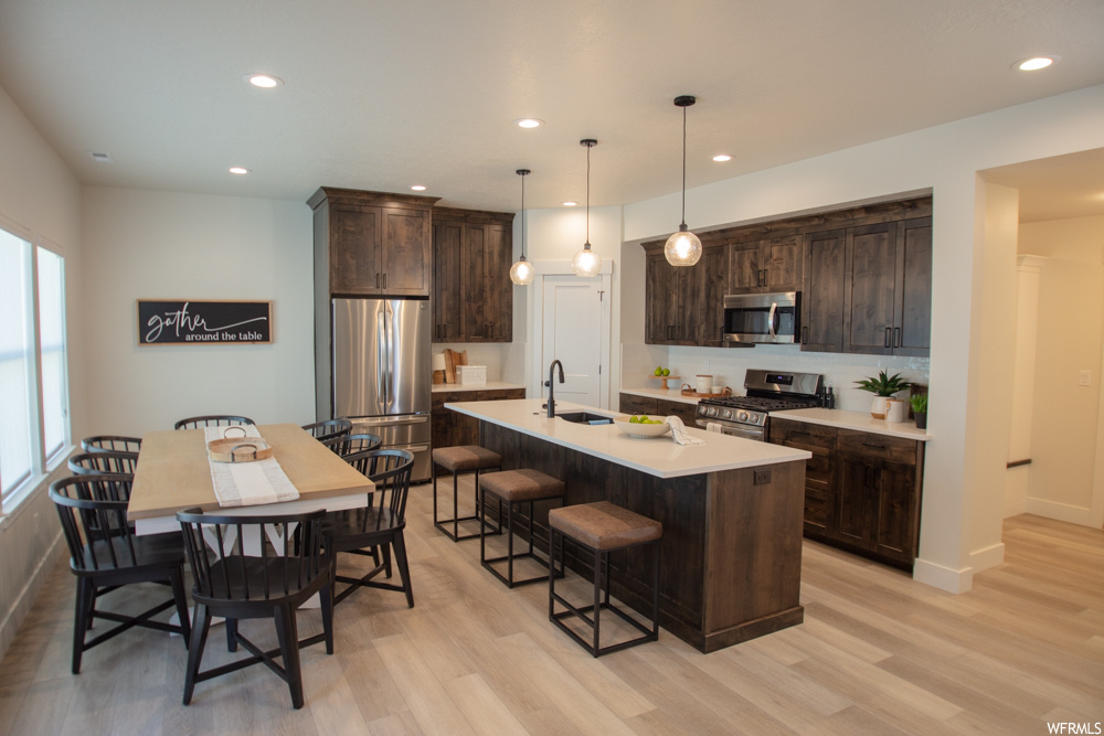 Kitchen with light hardwood / wood-style flooring, a center island with sink, and appliances with stainless steel finishes
