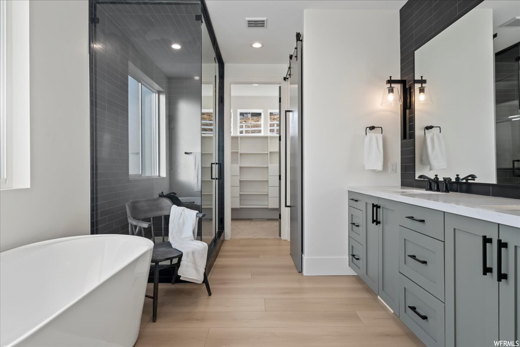 Bathroom with double sink, hardwood / wood-style flooring, a bath to relax in, and vanity with extensive cabinet space