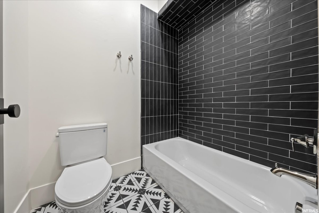 Bathroom with toilet, tiled shower / bath combo, and tile floors