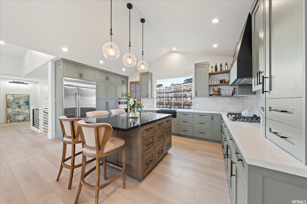 Kitchen featuring pendant lighting, custom exhaust hood, tasteful backsplash, light hardwood / wood-style flooring, and a kitchen island
