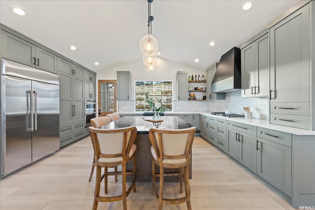 Kitchen featuring a kitchen island, appliances with stainless steel finishes, light hardwood / wood-style floors, and wall chimney range hood