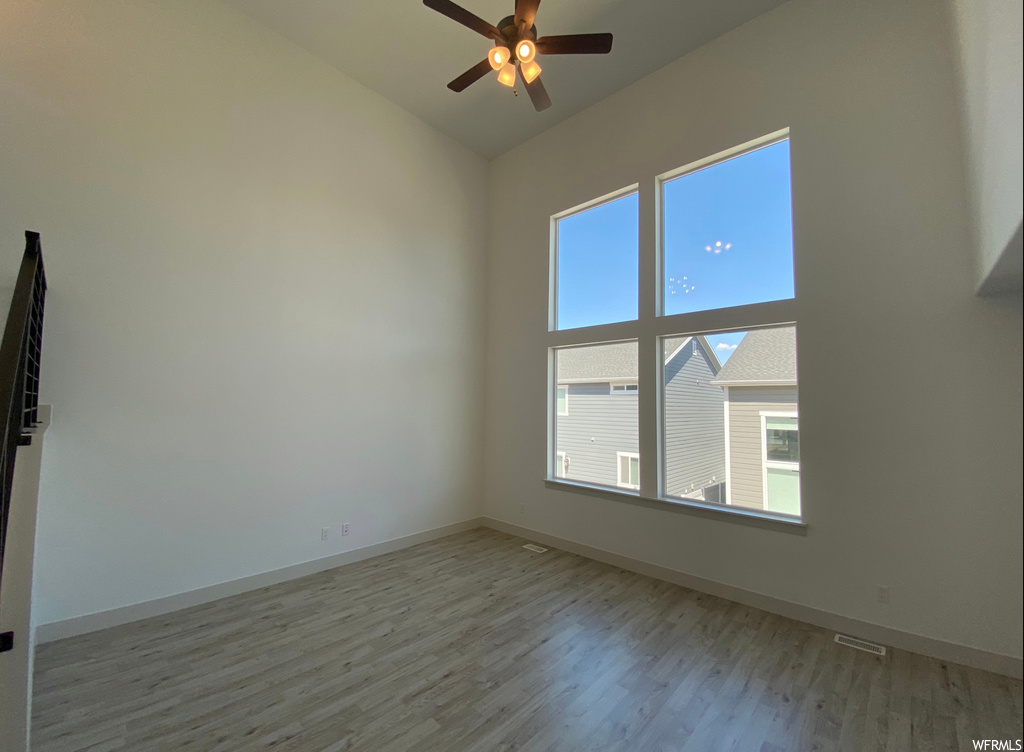 Empty room with a high ceiling, ceiling fan, and light hardwood / wood-style floors