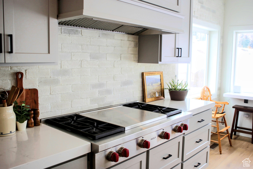 Kitchen featuring custom range hood, stainless steel gas stovetop, tasteful backsplash, and light hardwood / wood-style floors