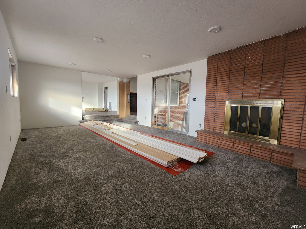 Unfurnished living room with a brick fireplace and carpet floors