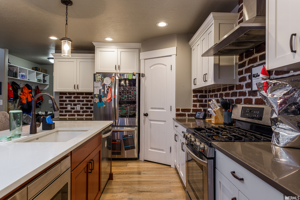 Kitchen featuring sink, light hardwood / wood-style flooring, appliances with stainless steel finishes, pendant lighting, and wall chimney exhaust hood
