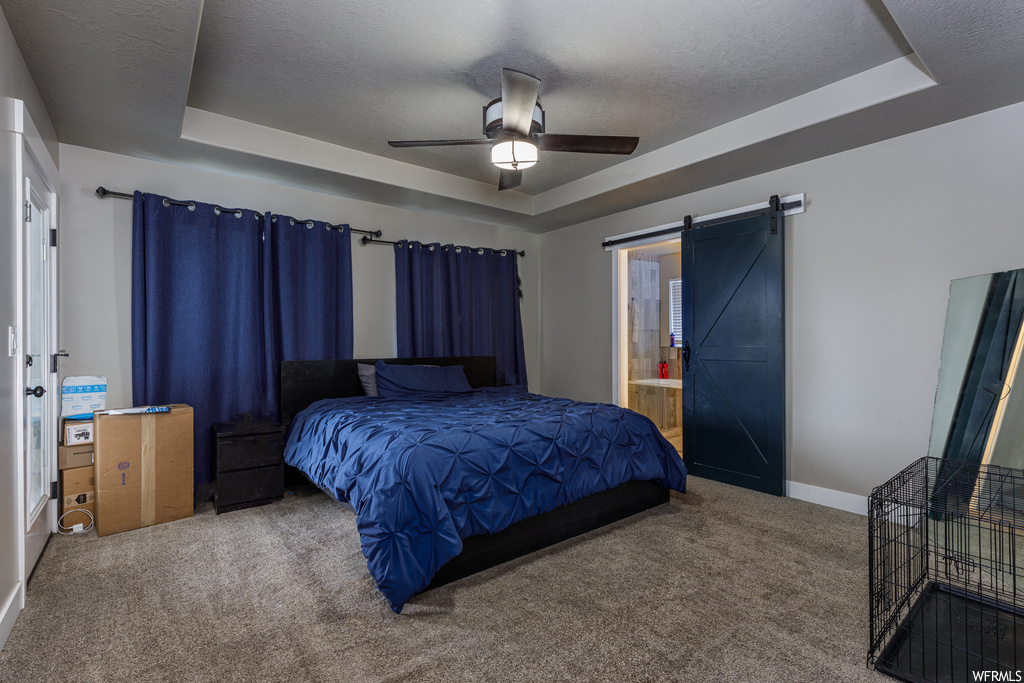 Carpeted bedroom with a tray ceiling, ensuite bathroom, ceiling fan, and a barn door
