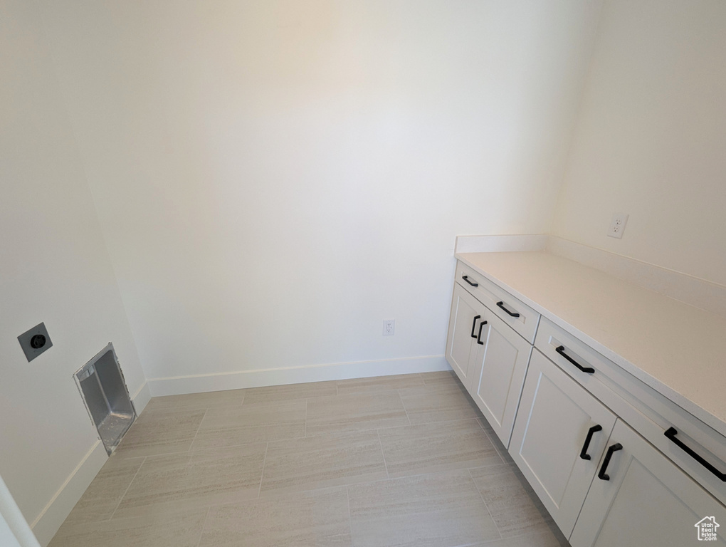 Laundry room featuring electric dryer hookup, cabinets, and light tile floors