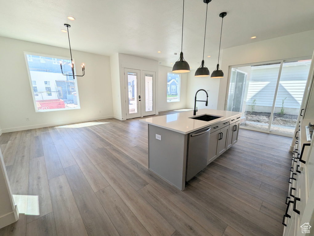 Kitchen with hardwood / wood-style floors, sink, decorative light fixtures, and a kitchen island with sink