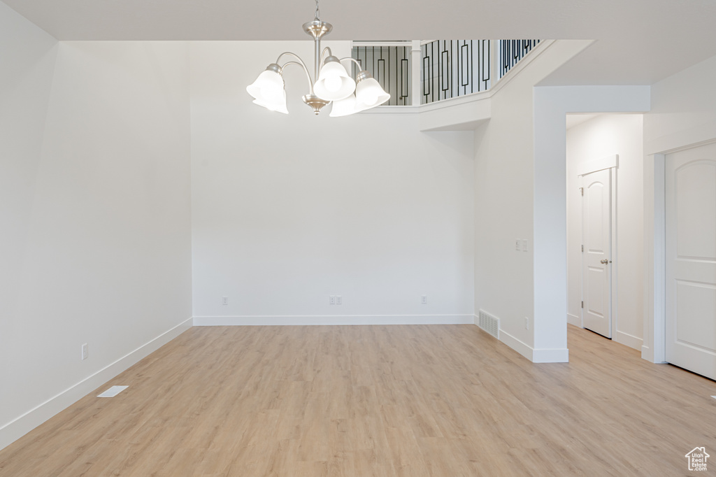 Empty room with light hardwood / wood-style floors and a notable chandelier