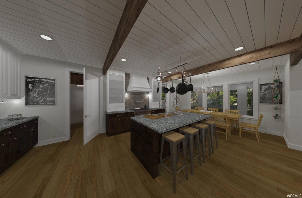 Kitchen with dark wood-type flooring, beamed ceiling, pendant lighting, custom exhaust hood, and a center island with sink