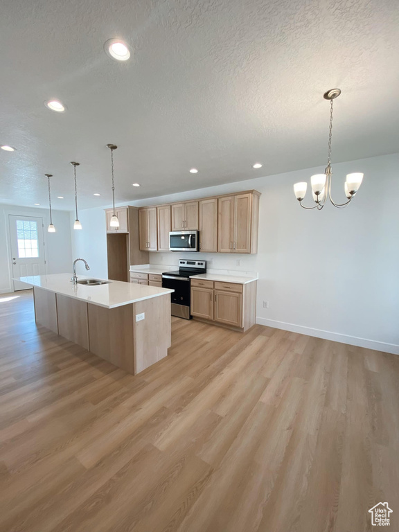 Kitchen with electric range oven, sink, pendant lighting, light wood-type flooring, and an island with sink