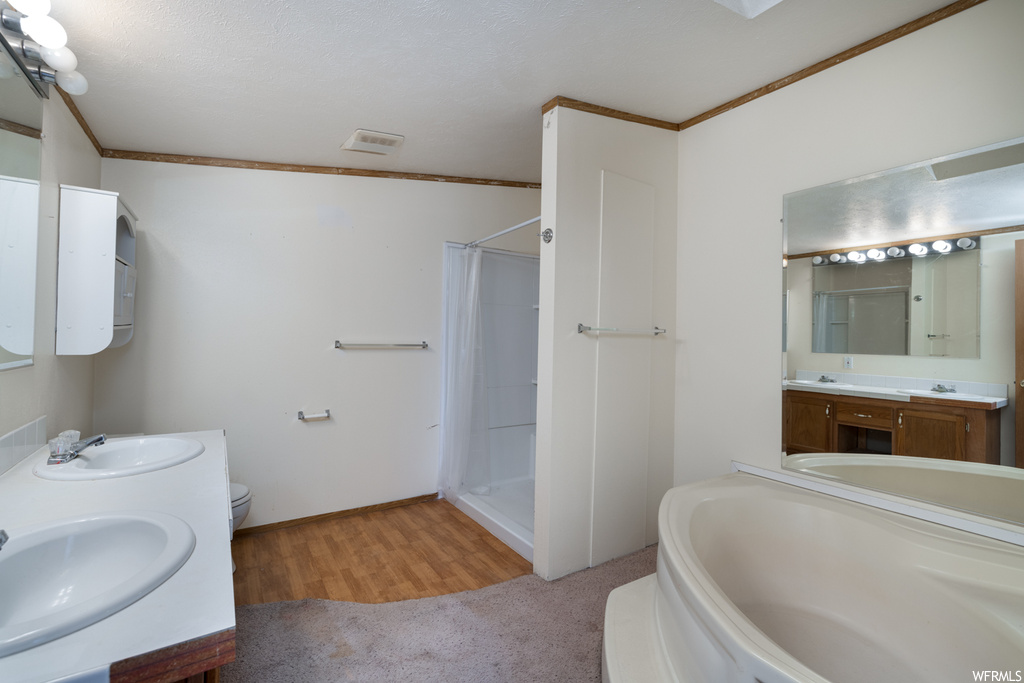 Full bathroom with toilet, hardwood / wood-style flooring, separate shower and tub, dual bowl vanity, and ornamental molding