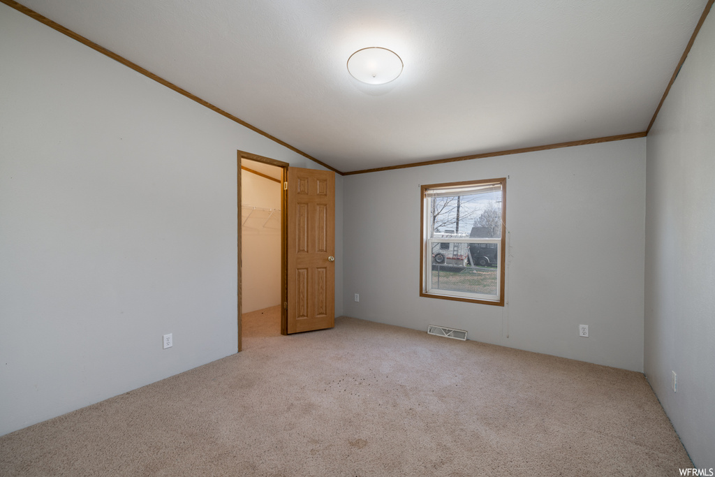 Unfurnished room featuring lofted ceiling, crown molding, and light colored carpet