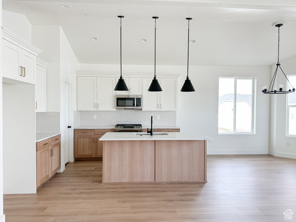 Kitchen featuring light wood-type flooring, appliances with stainless steel finishes, pendant lighting, and a center island with sink