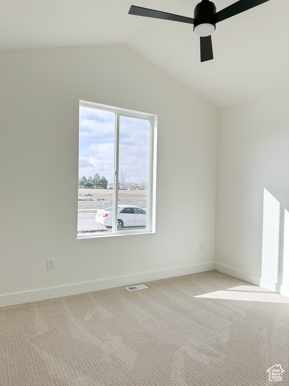 Empty room with vaulted ceiling, light carpet, and ceiling fan