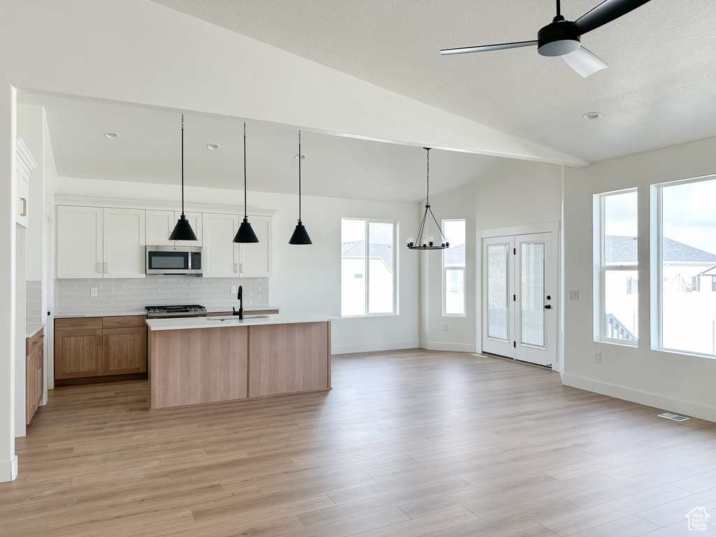 Kitchen with plenty of natural light, white cabinets, stainless steel appliances, and a kitchen island with sink