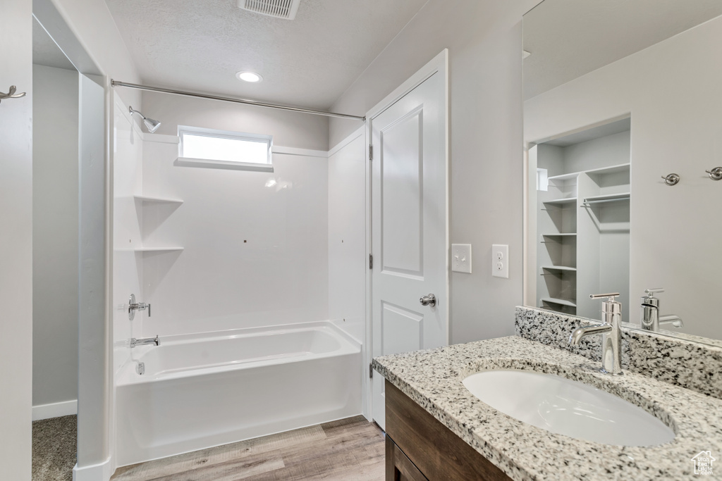 Bathroom with a textured ceiling, hardwood / wood-style floors, bathing tub / shower combination, and vanity with extensive cabinet space