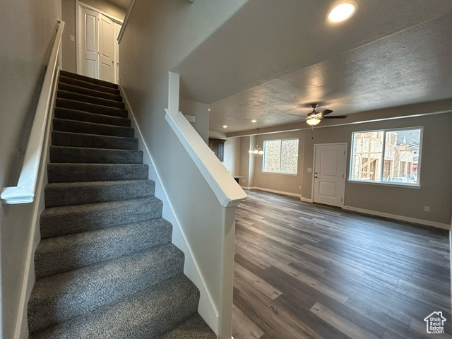 Stairs with a textured ceiling, ceiling fan, and dark wood-type flooring