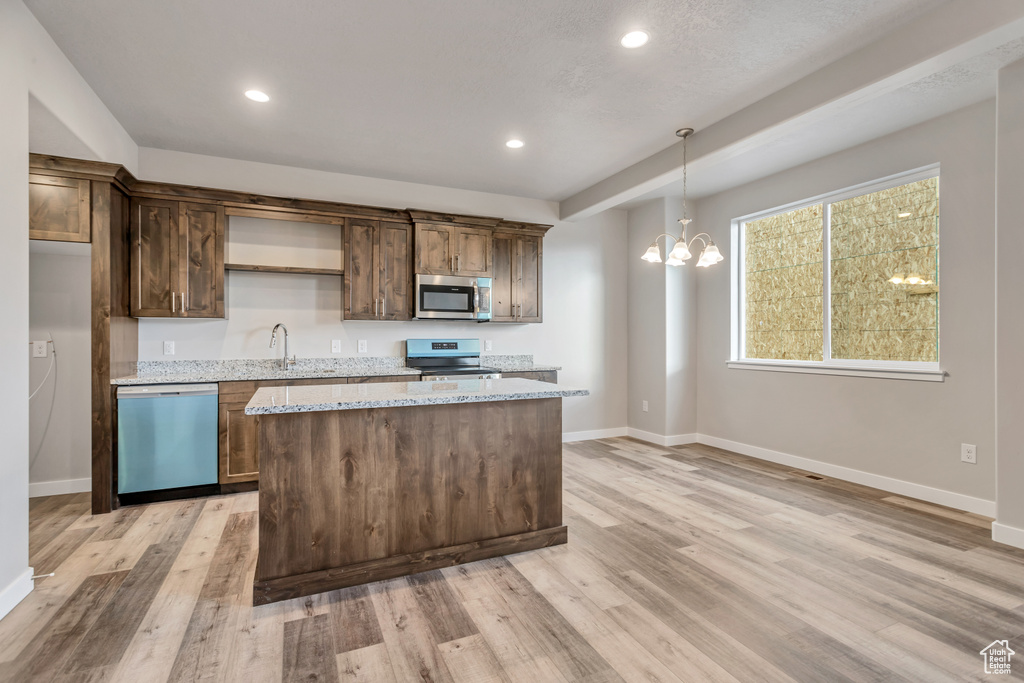 Kitchen with hanging light fixtures, light stone countertops, appliances with stainless steel finishes, a kitchen island, and light hardwood / wood-style floors
