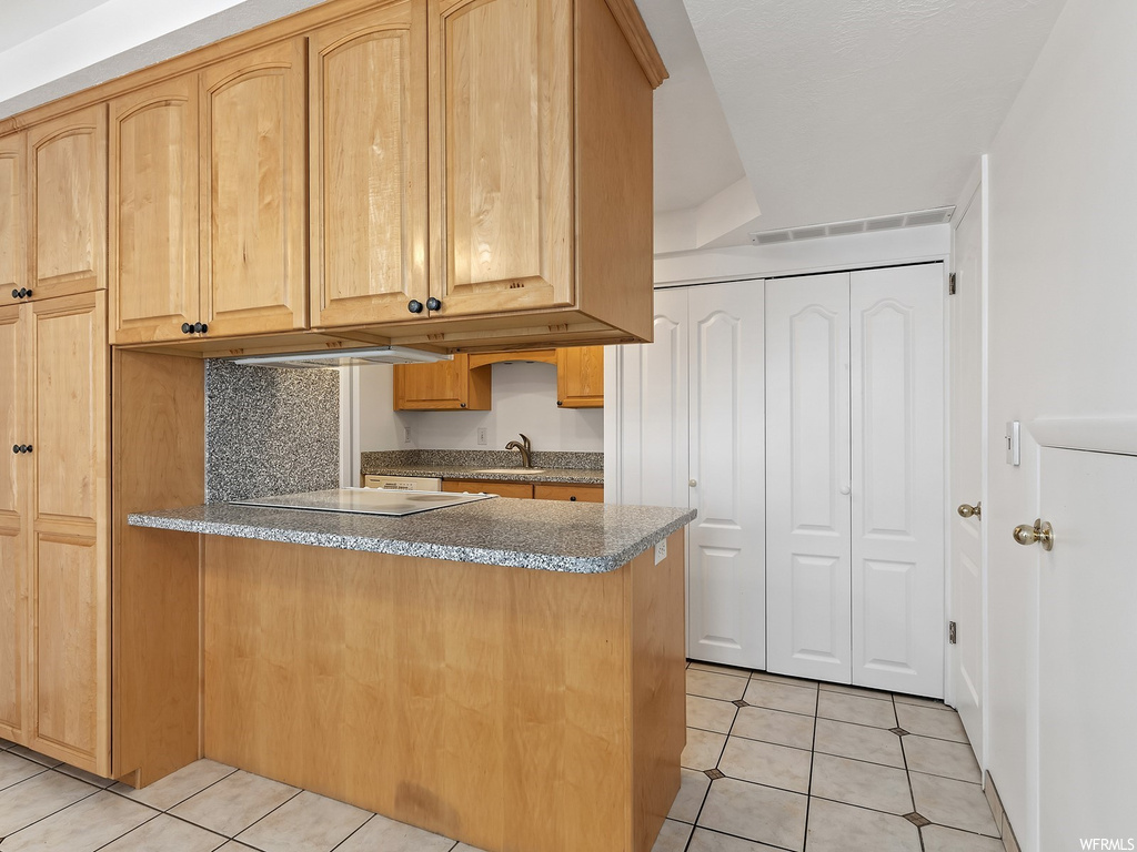 Kitchen featuring dark stone counters, light tile flooring, light brown cabinetry, and tasteful backsplash