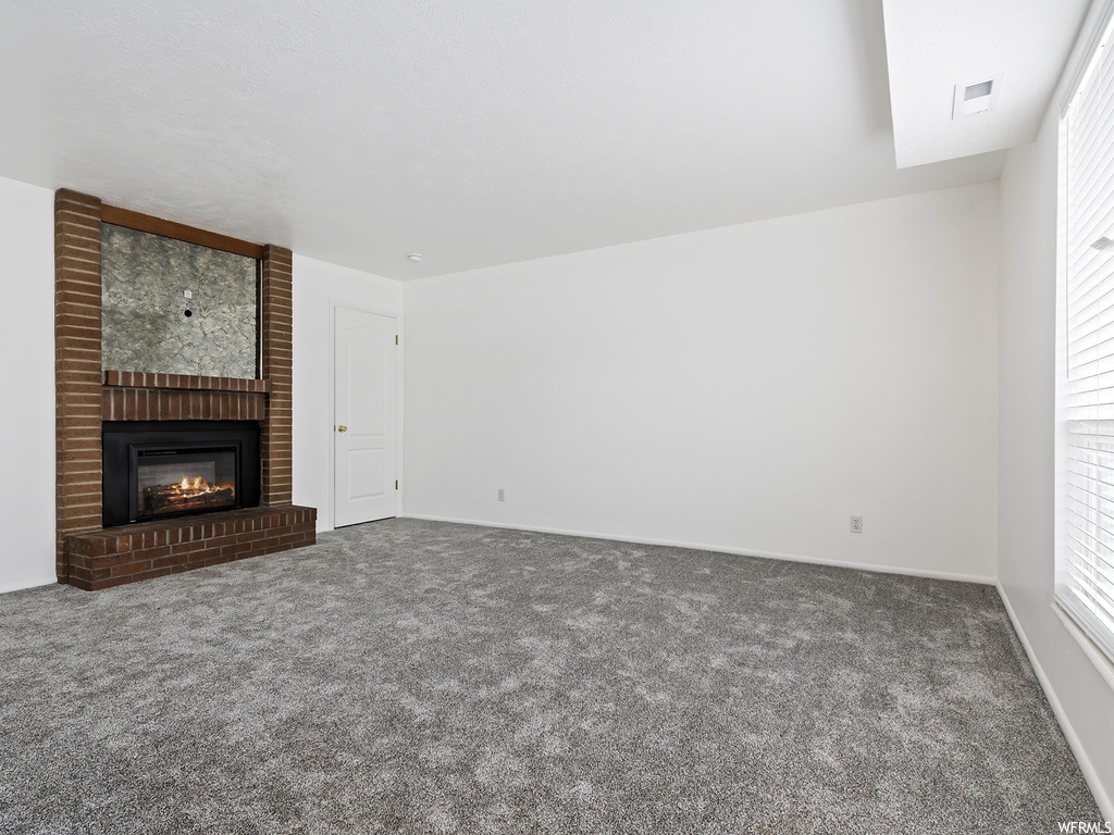Unfurnished living room with carpet, a fireplace, and brick wall