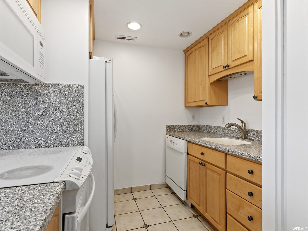 Kitchen with light tile flooring, sink, light stone countertops, tasteful backsplash, and white appliances