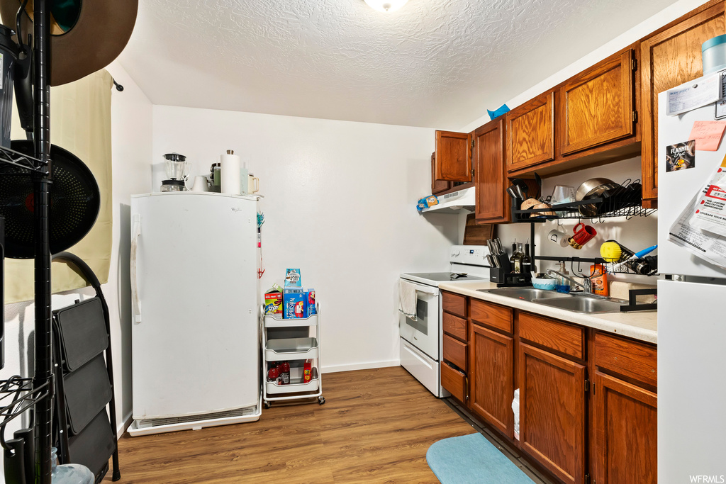 Kitchen with white appliances, a textured ceiling, light wood-type flooring, and sink