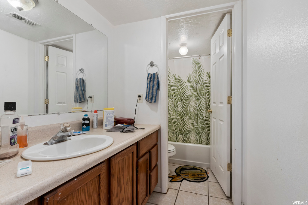 Full bathroom featuring toilet, tile floors, vanity with extensive cabinet space, and shower / bath combo