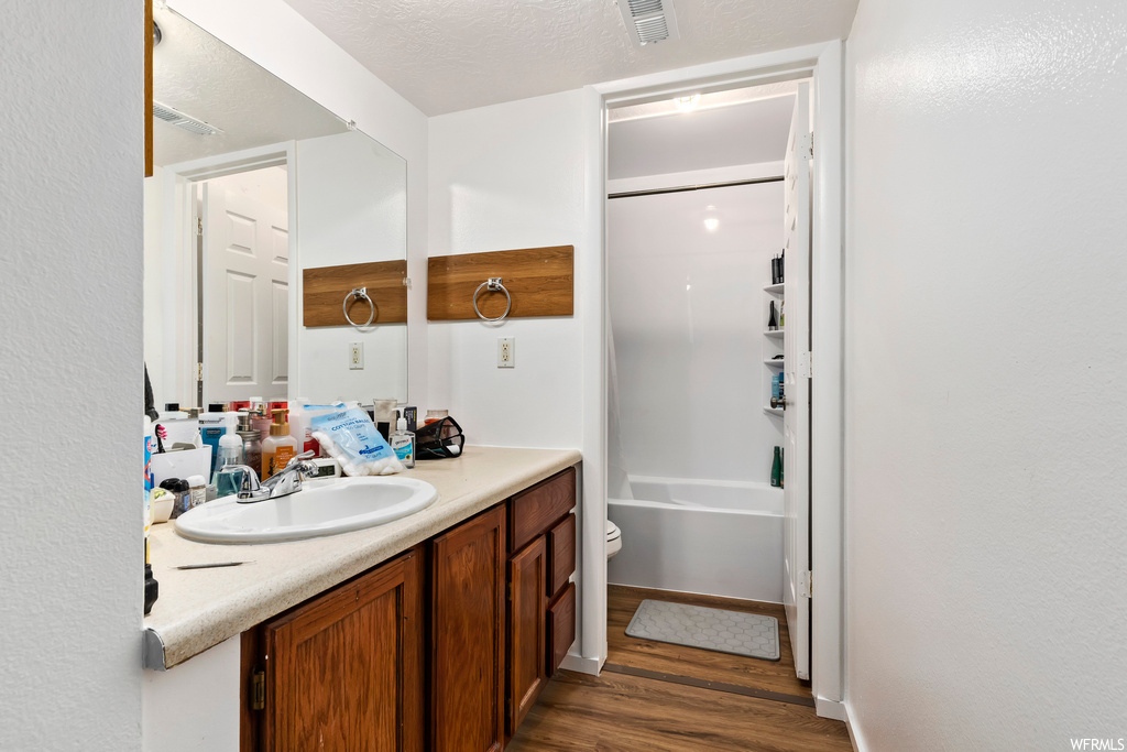 Full bathroom featuring toilet, a textured ceiling, vanity, bathtub / shower combination, and hardwood / wood-style floors