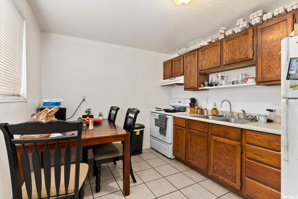 Kitchen featuring light tile floors, sink, white appliances, and a textured ceiling
