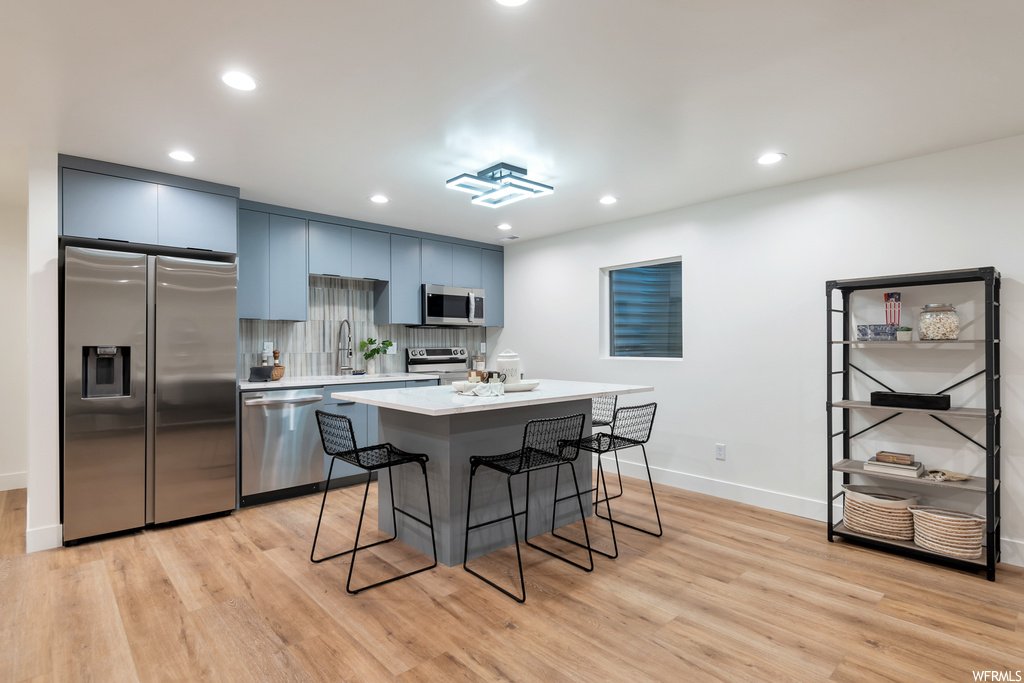 Kitchen with light hardwood / wood-style floors, a breakfast bar area, stainless steel appliances, backsplash, and a kitchen island