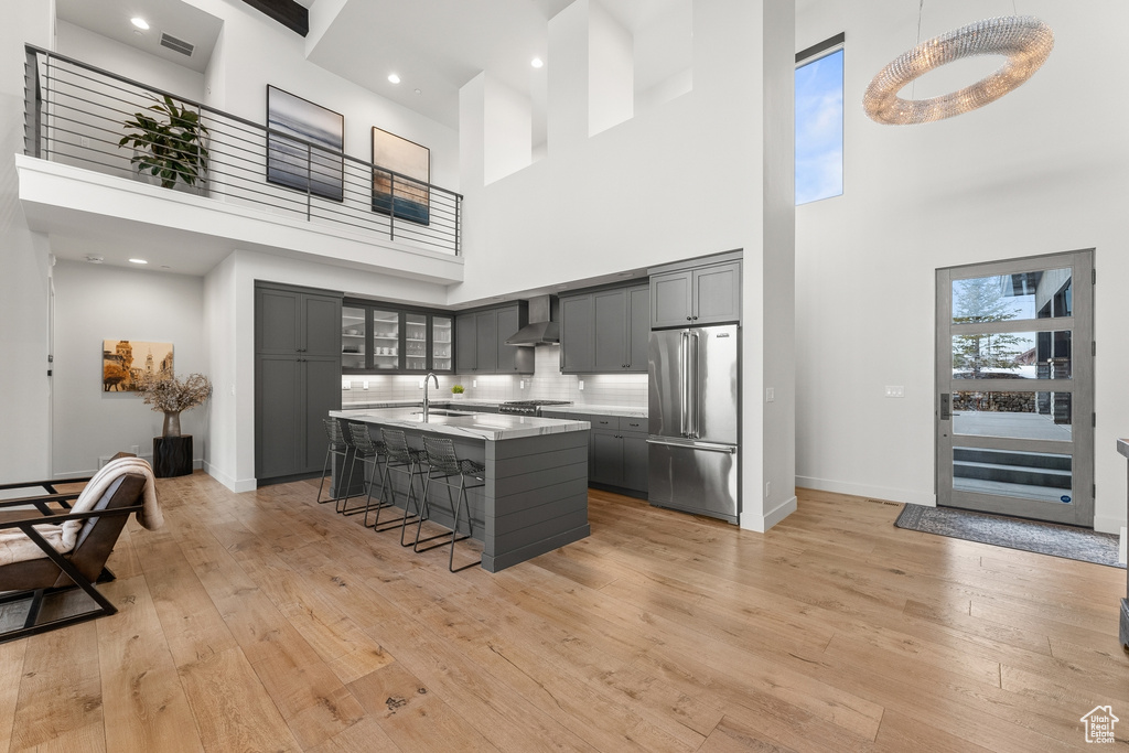 Kitchen with light wood-type flooring, appliances with stainless steel finishes, a high ceiling, and a kitchen breakfast bar