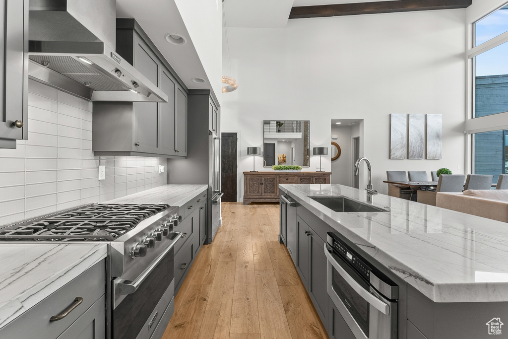 Kitchen featuring light hardwood / wood-style floors, high end range, wall chimney exhaust hood, sink, and gray cabinetry