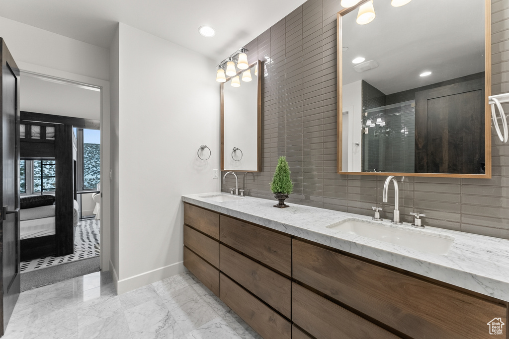 Bathroom featuring dual sinks, tile walls, vanity with extensive cabinet space, backsplash, and tile flooring