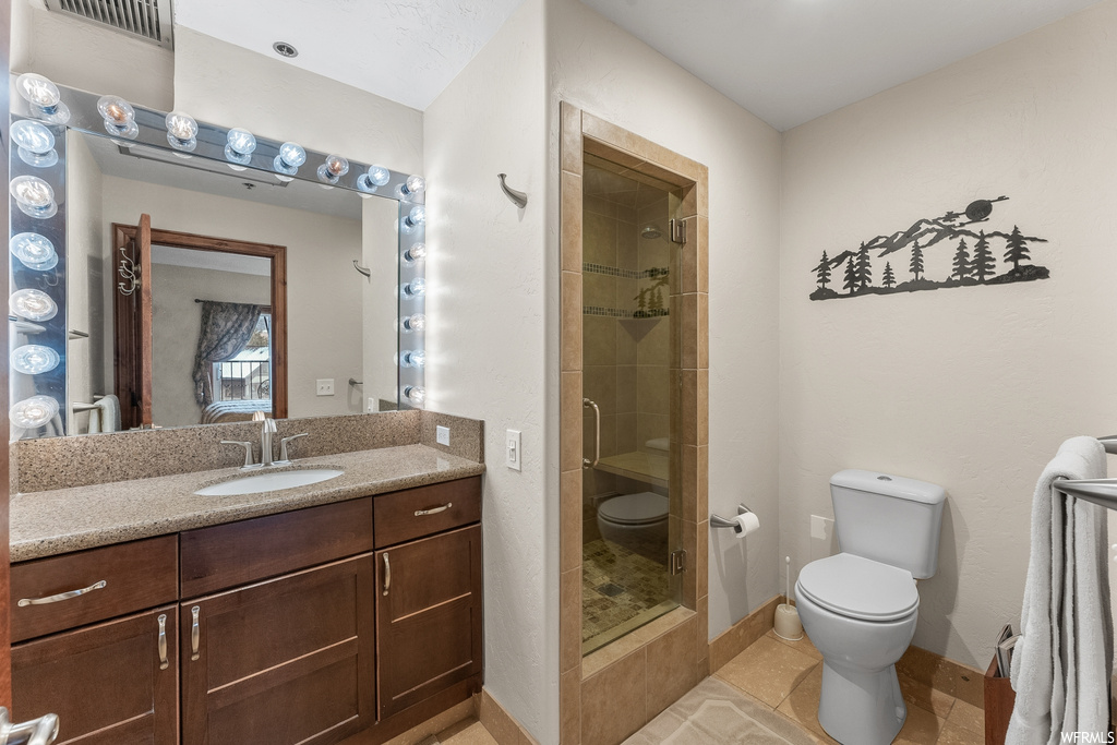 Bathroom with toilet, vanity with extensive cabinet space, an enclosed shower, and tile flooring