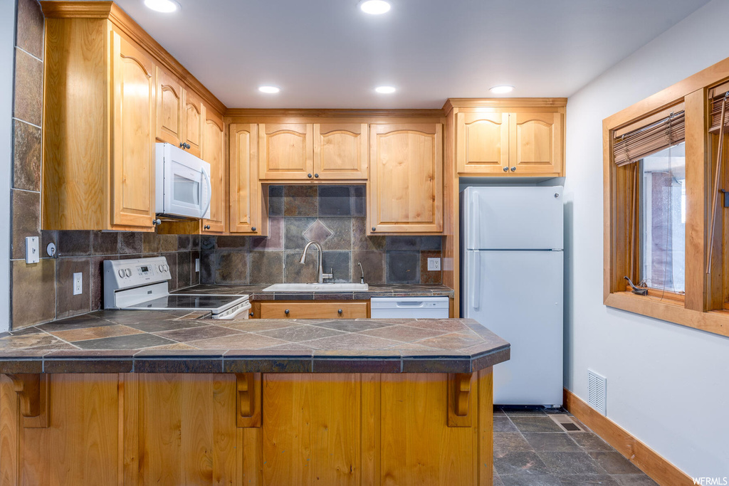 Kitchen with sink, dark tile floors, tile countertops, white appliances, and backsplash