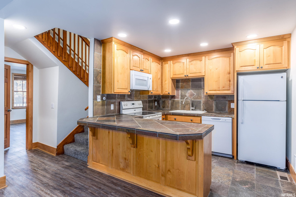Kitchen with tile counters, sink, tasteful backsplash, white appliances, and dark hardwood / wood-style floors