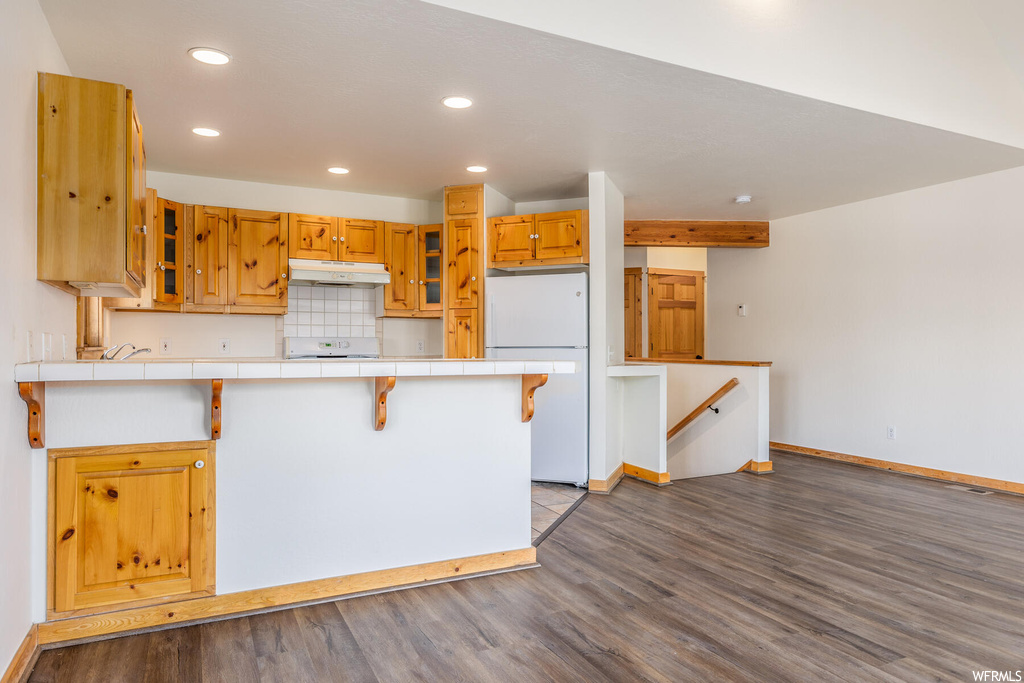 Kitchen with white refrigerator, light hardwood / wood-style flooring, range, tile counters, and backsplash