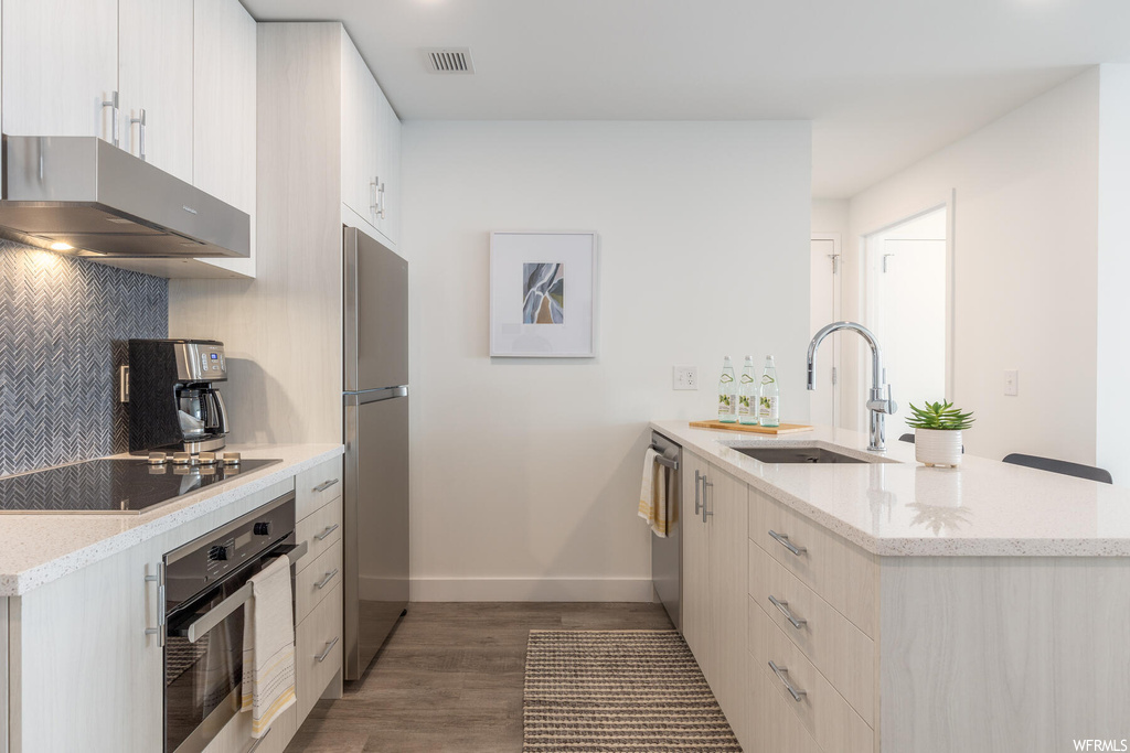 Kitchen with sink, wall chimney range hood, light hardwood / wood-style floors, stainless steel appliances, and backsplash